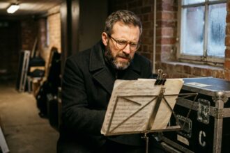 Musicien en tournée d'hiver portant des lunettes de vue et lisant une partition musicale dans les coulisses d'une salle de concert